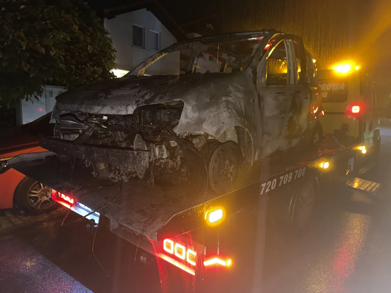 Spalony samochód zabezpieczony na autolawecie po zmroku